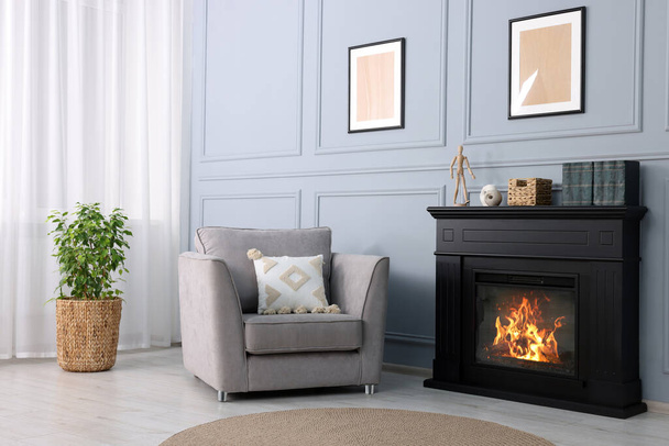 Black stylish fireplace near potted plant and armchair in cosy living room - Fotografie, Obrázek