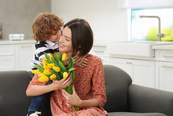 Little son congratulating his mom with Mother`s day at home, space for text. Woman holding bouquet of yellow tulips - Fotoğraf, Görsel