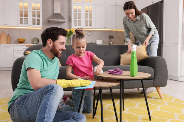 Spring cleaning. Parents with their daughter tidying up living room together - 写真・画像