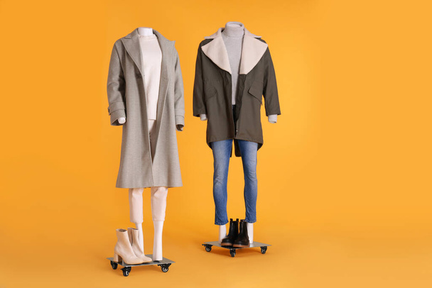 Mannequins with boots dressed in stylish coat, jacket, sweater and turtleneck on orange background - Фото, изображение