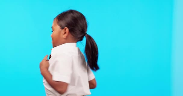 Ευτυχισμένος, περιστροφή και τη στολή ενός παιδιού σε ένα μπλε φόντο για το σχολείο, την εκπαίδευση και την προβολή πουκάμισο. Χαμόγελο, χώρος και πρόσωπο πορτραίτο ενός κοριτσιού με φοιτητικά ρούχα απομονωμένο σε σκηνικό στούντιο μακιγιαρίσματος. - Πλάνα, βίντεο