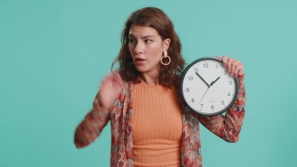 Woman with anxiety checking time on clock, running late to work, being in delay, deadline. Brunette busy girl looking at hour, minutes, worrying to be punctual isolated on blue studio background - Footage, Video