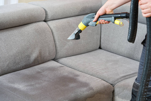 Dry cleaners man employee removing dirt from furniture in flat, closeup, vacuum clean sofa with professional equipment. cleaning sofa with washing suction cleaner closeup. - Photo, Image