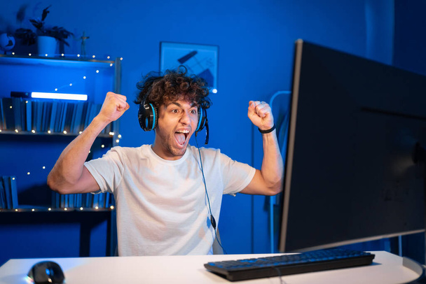 Arabische junge männliche Spieler gewinnen in Online-Videospiel auf dem Computer. Porträt eines Mannes mit Kopfhörer, der ein PvP-Turnier gewinnt. Kopierraum - Foto, Bild