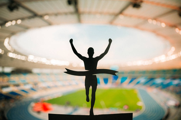 Triumph of Speed: Silhouette of Runner Soars to Victory at Modern Athletics Stadium. Edit Space, Track and Field Competition Photo. - Foto, afbeelding