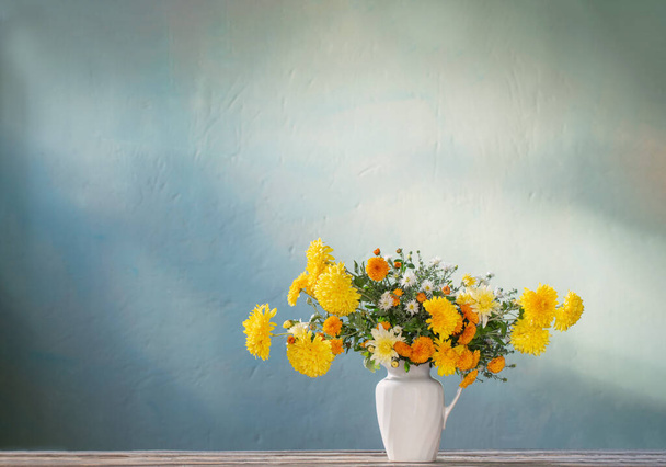 yellow and white chrysanthemum in white jug on wooden table - Foto, Imagen