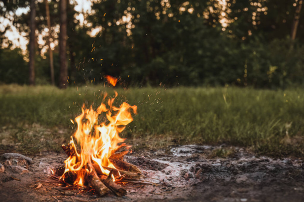 Yksinäinen ilta metsäleirinuotion ääressä - Luonnon kauneuden syleily tulen palaessa lähellä jokea, lumoavaa iltataivasta vastaan - Valokuva, kuva