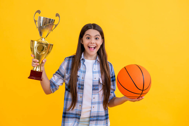 successful proud teen basketball girl with champion cup award. teen basketball girl hold award cup isolated on yellow. teen basketball girl receive award in studio. teen basketball girl accept award. - Photo, Image