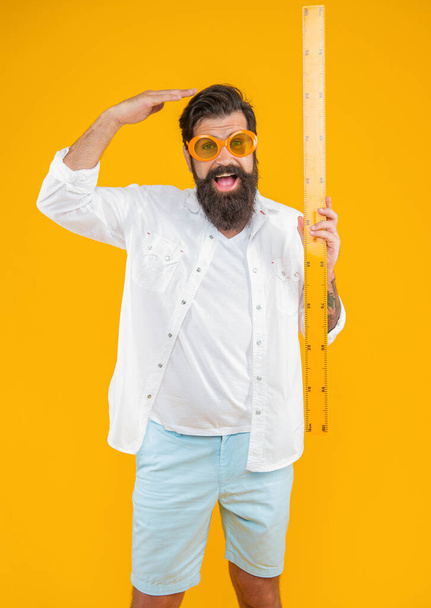 man hold measuring ruler shocked with height on background. photo of man hold measuring ruler. man hold measuring ruler isolated on yellow. man hold measuring ruler in studio. - 写真・画像