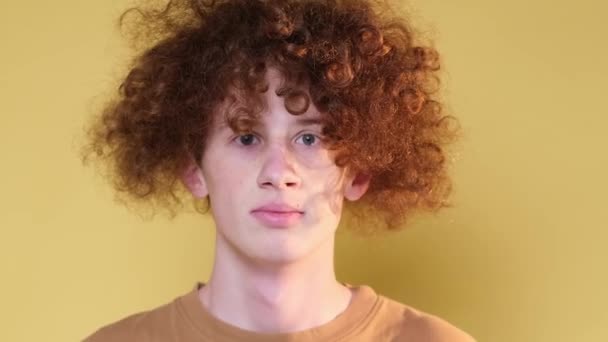Emotions of surprise of a modern young man at the camera. Red-haired curly guy shows surprise while standing on brown background. - Footage, Video