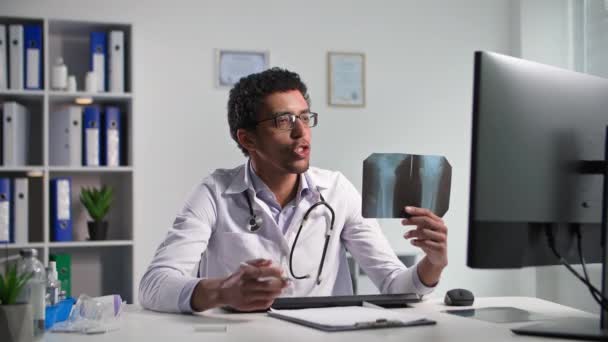 aanvaarding van patiënten online, een jonge zwarte arts met behulp van een video-oproep en toont x-ray terwijl zittend in een Melecian kantoor - Video