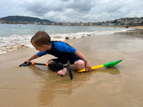 un niño buscando tesoros en la playa, con un detector de metales - Foto, Imagen