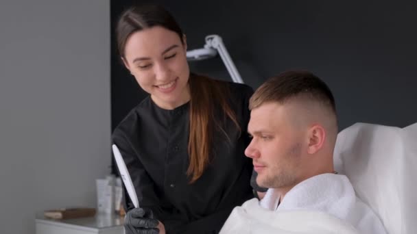 Um cliente satisfeito no esteticista olha no espelho o resultado de uma massagem facial. Cosmetologia masculina - Filmagem, Vídeo