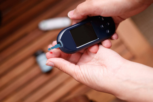 Women using glucometer, checking blood sugar level. Diabetes concept on brown background - Fotografie, Obrázek