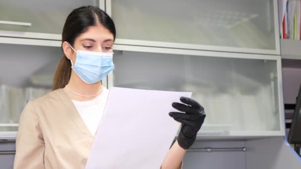 Жінка-стоматолог у масці дивиться на рентгенівське зображення пацієнта, стоячи в її кабінеті. Сучасна стоматологія. Жіночий стоматолог
 - Кадри, відео