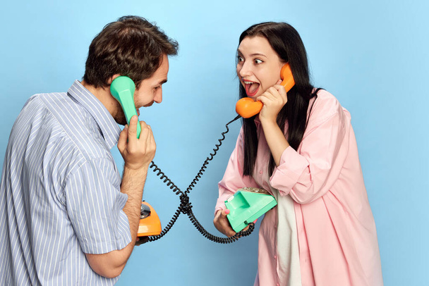 Alegre joven hombre y mujer emocionalmente hablando por teléfono contra fondo azul estudio. Riendo y divirtiéndose. Concepto de amistad, relación, comunicación, emociones, estilo de vida, anuncio - Foto, imagen