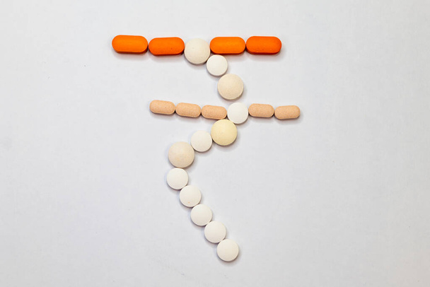A close-up photo of a few health care pills in the shape of the Indian rupee symbol on a white background. - Photo, image