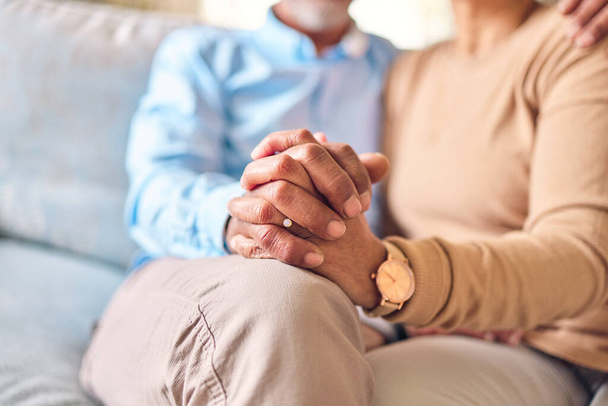 Love, support and a senior couple holding hands while sitting on a sofa in the living room of their home during retirement. Trust, relax or affection with an elderly man and woman bonding together. - Foto, Imagem