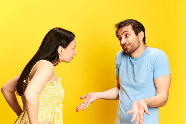 Young woman emotionally talkin to man, asking questions against yellow studio background. Man making excuses. Concept of friendship, relationship, communication, emotions, lifestyle, ad - Photo, Image