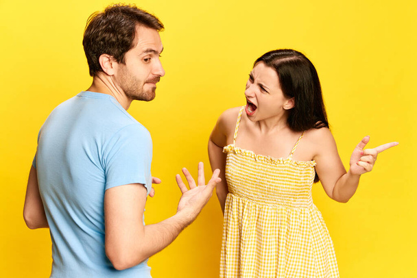 Couple quarrels. Being jealous. Woman emotionally talking, shouting to man, complaining against yellow studio background. Concept of friendship, relationship, communication, emotions, lifestyle, ad - Foto, Bild