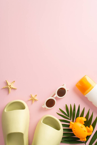 A bird's-eye vertical view of summer escape with kids, showcasing starfish, beach toys, slippers, sunglasses, sunscreen and palm leaf on pink isolated background, with empty space for text or advert - Foto, afbeelding