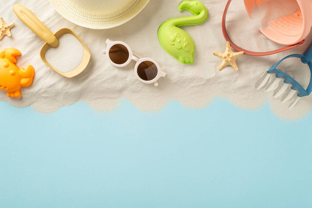 Beach relaxation on the seaside with children. Top view photo of sand with sand toys for kids, panama and sunglasses and starfish on isolated blue background with copyspace - Photo, Image