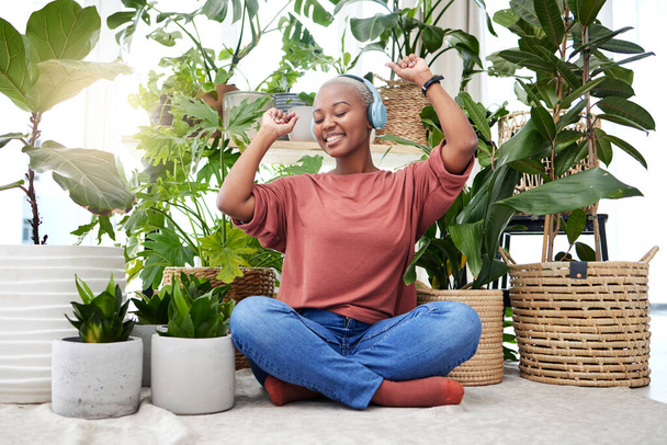 Music, dance and radio with a black woman in her home by plants while streaming an audio playlist. Freedom, headphones and subscription service with a carefree young female person in her house. - Foto, afbeelding