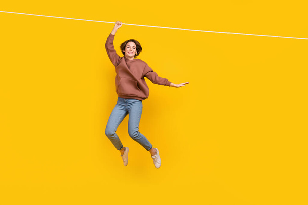 Full body photo of young charming lady hanging ropes lightness careless wear trendy clothes shopping ad isolated on yellow color background. - Фото, изображение