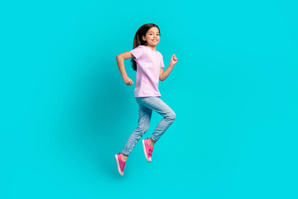 Full body photo of small girl run fast speed have fun wear pink t-shirt jeans hurry after school isolated on aquamarine color background. - 写真・画像