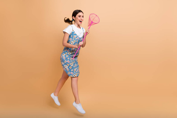 Full length photo of cute pretty lady wear flower print dress jumping hunting butterflies empty space isolated beige color background. - Fotoğraf, Görsel