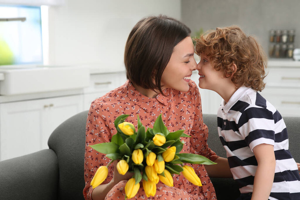 Little son congratulating his mom with Mother`s day at home. Woman holding bouquet of yellow tulips - Zdjęcie, obraz