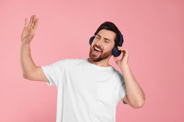 Emotional man listening music with headphones on pink background - Foto, afbeelding
