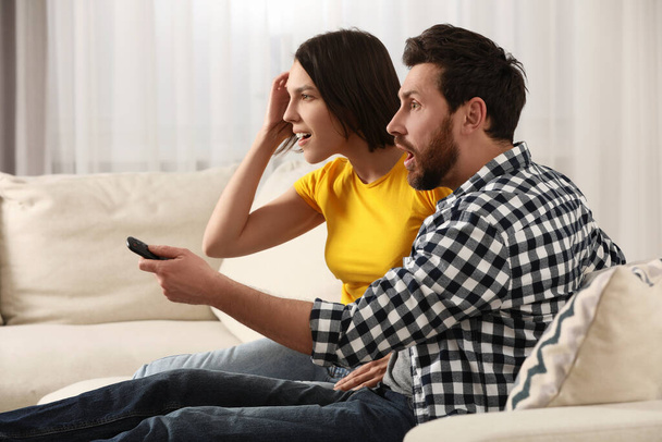 Surprised couple watching TV on sofa at home - Φωτογραφία, εικόνα