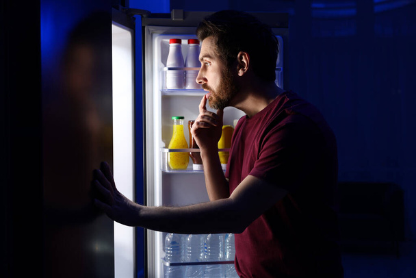 Чоловік вибирає їжу з холодильника на кухні вночі. Погана звичка
 - Фото, зображення