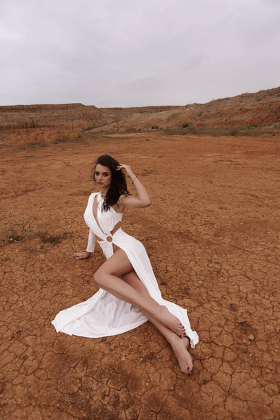 fashion outdoor photo of beautiful woman with dark hair in luxurious white dress with accessories posing in desert in Cyprus - Photo, image