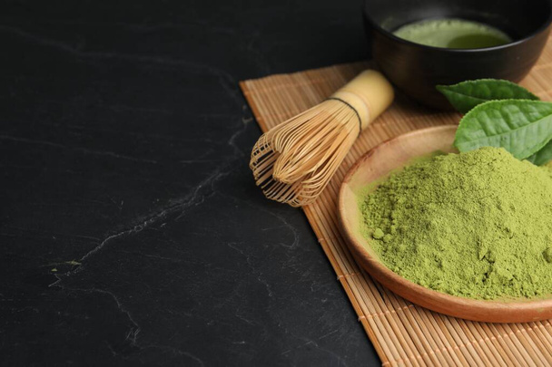 Green matcha powder and bamboo whisk on black table, closeup. Space for text - Photo, image