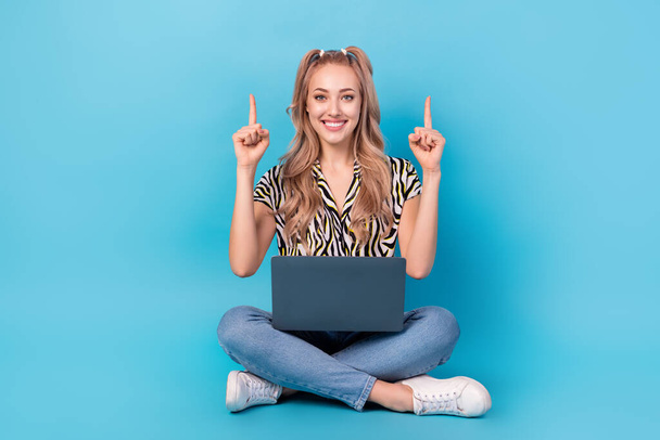 Full length photo of adorable girl dressed striped blouse sit with laptop directing at offer empty space isolated on blue color background. - 写真・画像