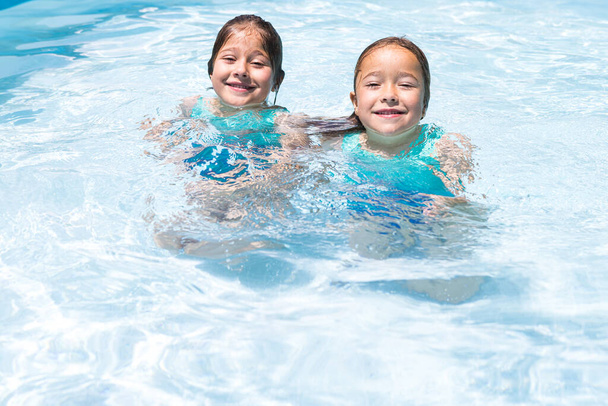 Two girls, in a pool, smiling, enjoying themselves in the water. Pool, swimming, swimsuit, children, summer, relax, vacation, resort and travel concept. - Foto, afbeelding