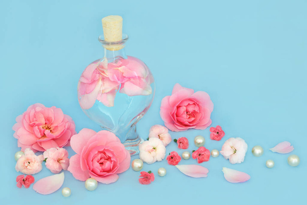 Woda różana do pielęgnacji skóry z kwiatami róż i goździków, butelka w kształcie serca i perły na niebiesko. Równoważy naturalne oleje do skóry, zmniejsza zaczerwienienie, naturalnie nawilża skórę leczy wysypki. - Zdjęcie, obraz