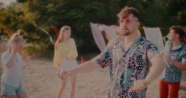 Lassú felvétel fiatal gondtalan férfi visel napszemüveg tánc barátok ellen a háttérben a hétvégi party a strandon - Felvétel, videó