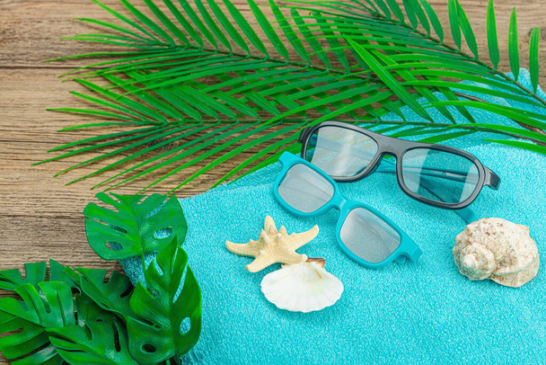 Koncept letních prázdnin. Ručník, sluneční brýle, mořská výzdoba. Palmové a monstera listy, dřevěné pozadí, ploché ležel, kopírovací prostor - Fotografie, Obrázek