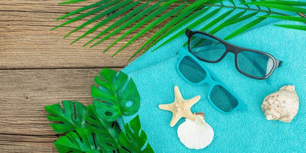 Summer vacation concept. Bath towel, sunglasses, marine decor. Palm and monstera leaves, wooden background, flat lay, banner format - Photo, Image