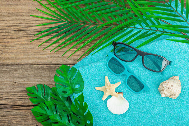 Летние каникулы. Ванное полотенце, солнцезащитные очки, морской декор. Листья пальмы и чудовища, деревянный фон, плоская кладка, вид сверху - Фото, изображение