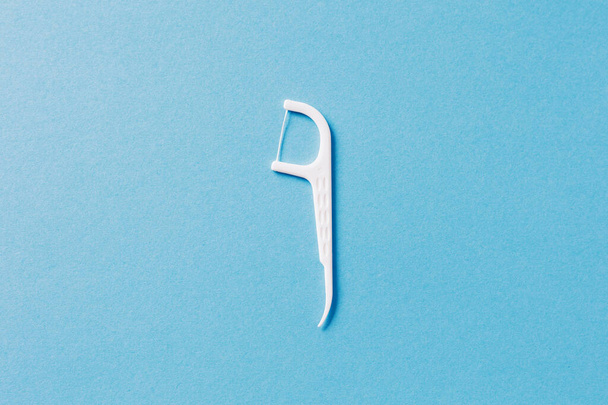 Πλαστική λευκή οδοντογλυφίδα με οδοντικό νήμα σε μπλε φόντο - Φωτογραφία, εικόνα
