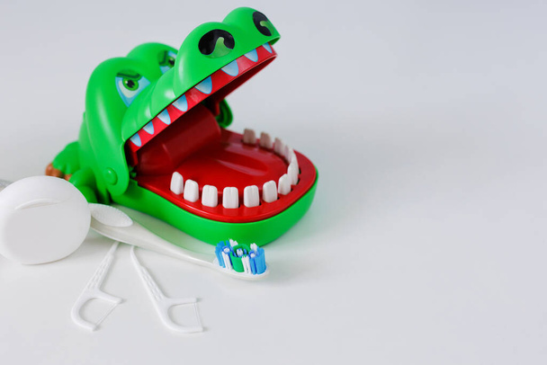 Οδοντικό νήμα, οδοντογλυφίδες, πινέλο και πράσινο κροκόδειλο σε λευκό φόντο - Φωτογραφία, εικόνα
