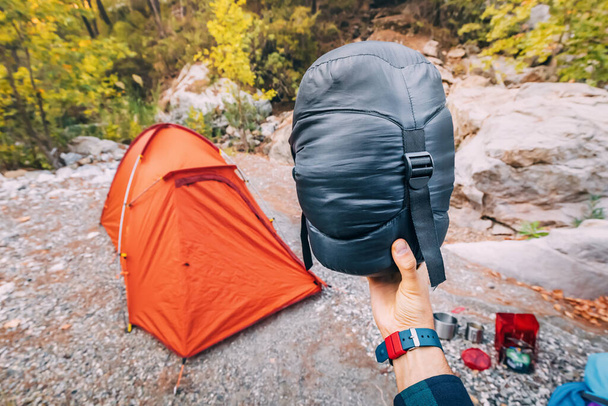Lichtgewicht en kleine compressie tas met een donzen slaapzak op de achtergrond van een tent op een camping en diverse kampeerspullen en items - Foto, afbeelding