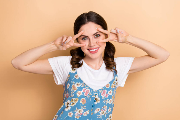 Photo of toothy beaming optimistic girl with curly ponytails wear blue overall showing v-sign on eyes isolated on pastel color background. - Foto, Imagem