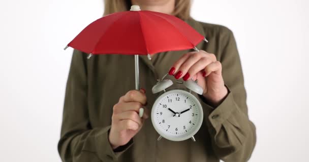 Woman is holding alarm clock and red umbrella. Protecting safety and saving time - Footage, Video