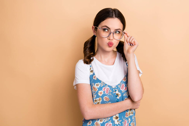 Photo of unsure suspicious girl dressed flower print overall arm eyewear looking empty space isolated beige color background. - Zdjęcie, obraz