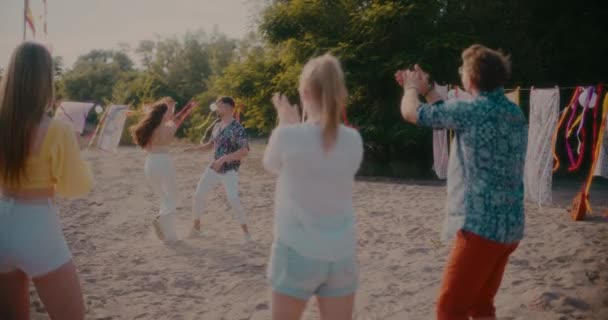 Genç arkadaşlar el çırpıyor ve yaz partisinde plajda dans eden neşeli çiftler. - Video, Çekim